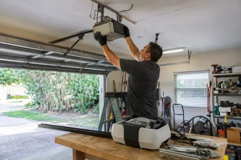 Person holding an overhead garage-door opener beside another opener and hardware on a workbench — Garage Door Opener Replacement, Welland