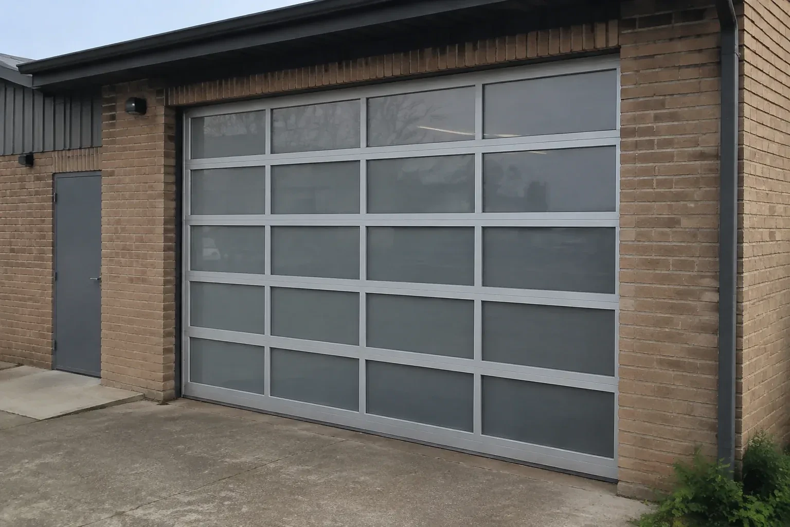 Closed glazed sectional door in a grey metal frame at a brick workshop. — Full-View Glass Garage Door Installation, Welland