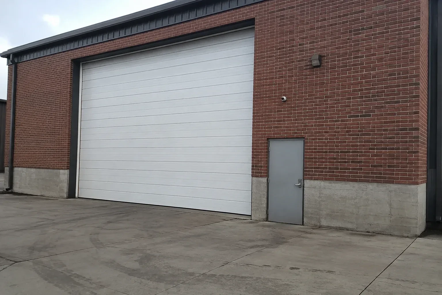 Tall closed sectional loading door beside a personnel door at a brick unit. — Commercial Sectional Door Repair, Welland